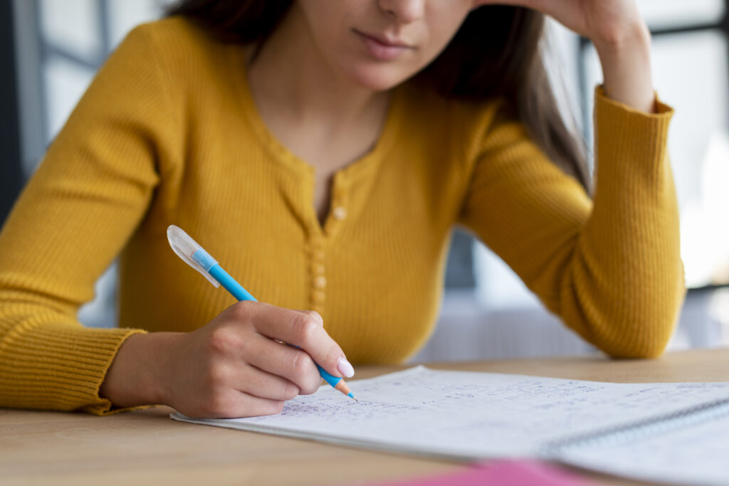 Mulher jovem estudando, segurando uma caneta azul e fazendo anotações em caderno, representando preparação para concurso público.